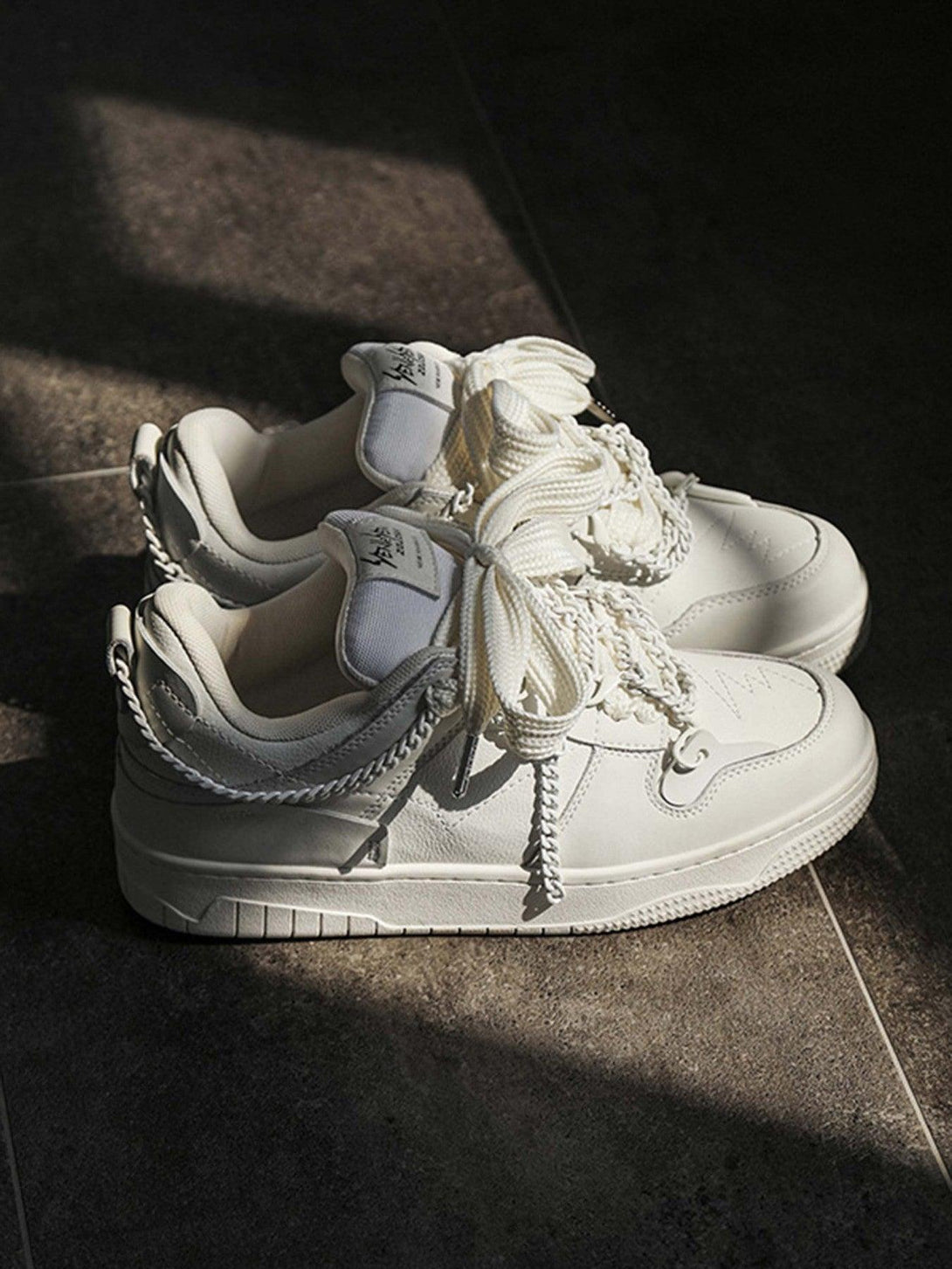 White TALISHKO sneakers with chain details showcased in a soft-lit, stylish setting.
