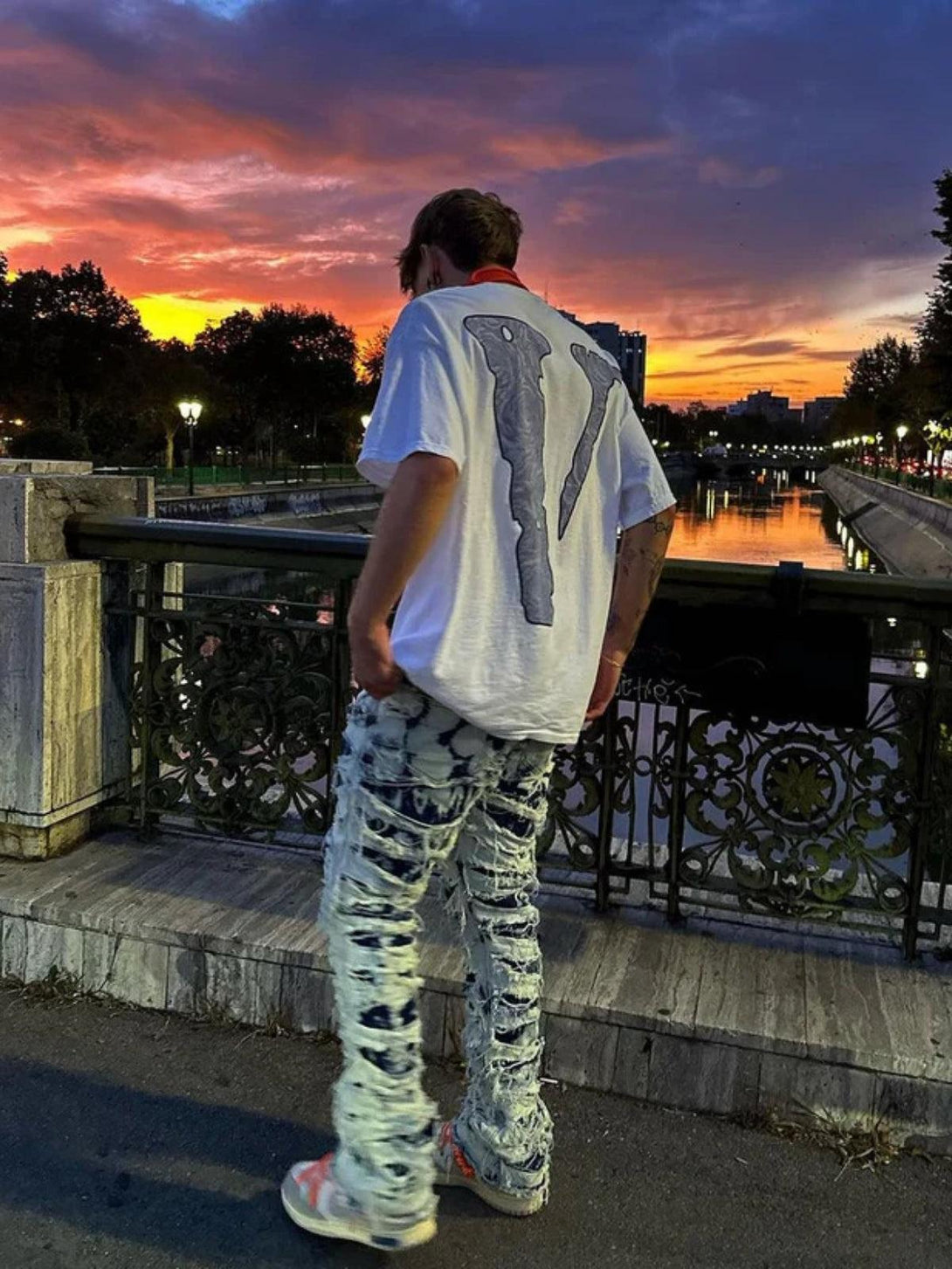 Man in TALISHKO distressed jeans, enjoying a sunset by the river, styled with casual flair.