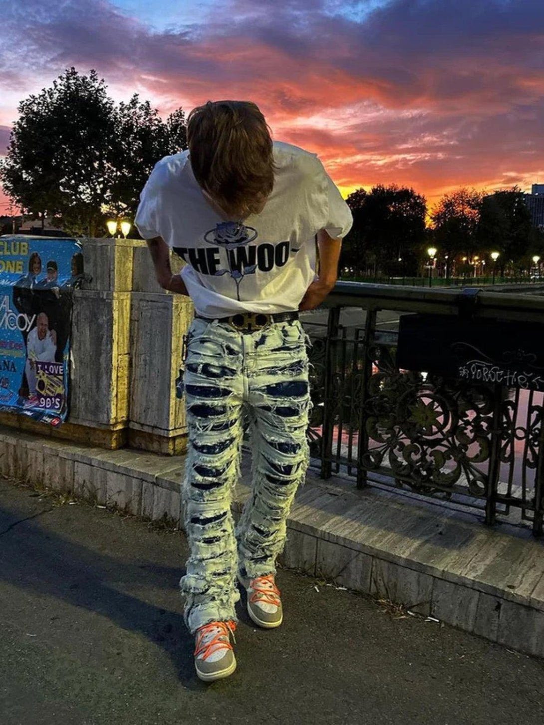 Model wearing TALISHKO distressed slim fit jeans, capturing urban style against a sunset backdrop.
