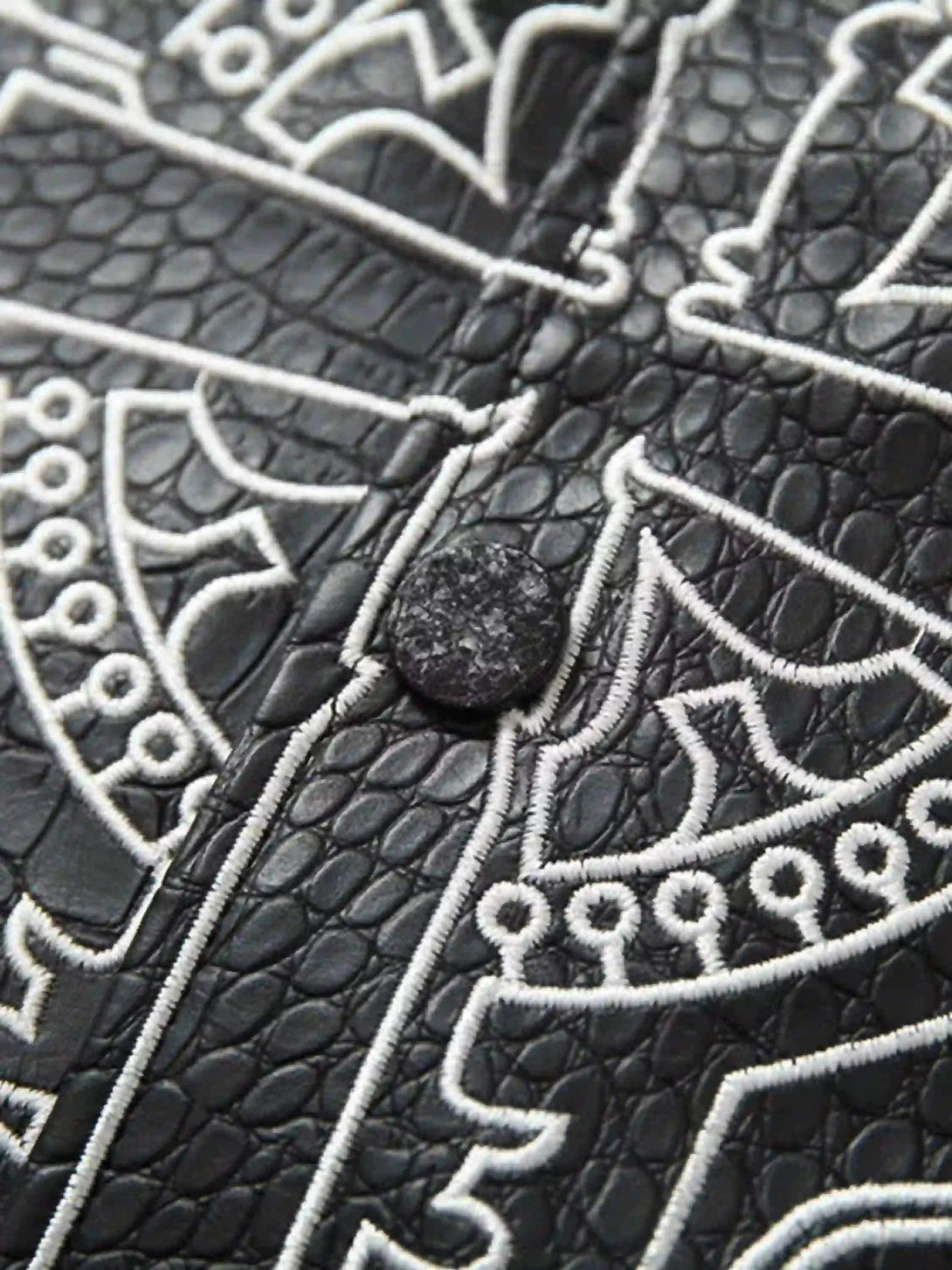 A detailed view of TALISHKO jacket's embossed leather texture with intricate gothic embroidery.