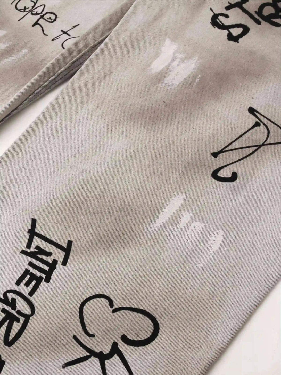 Intricate look at TALISHKO graffiti distressed jeans, featuring bold black text and unique designs.