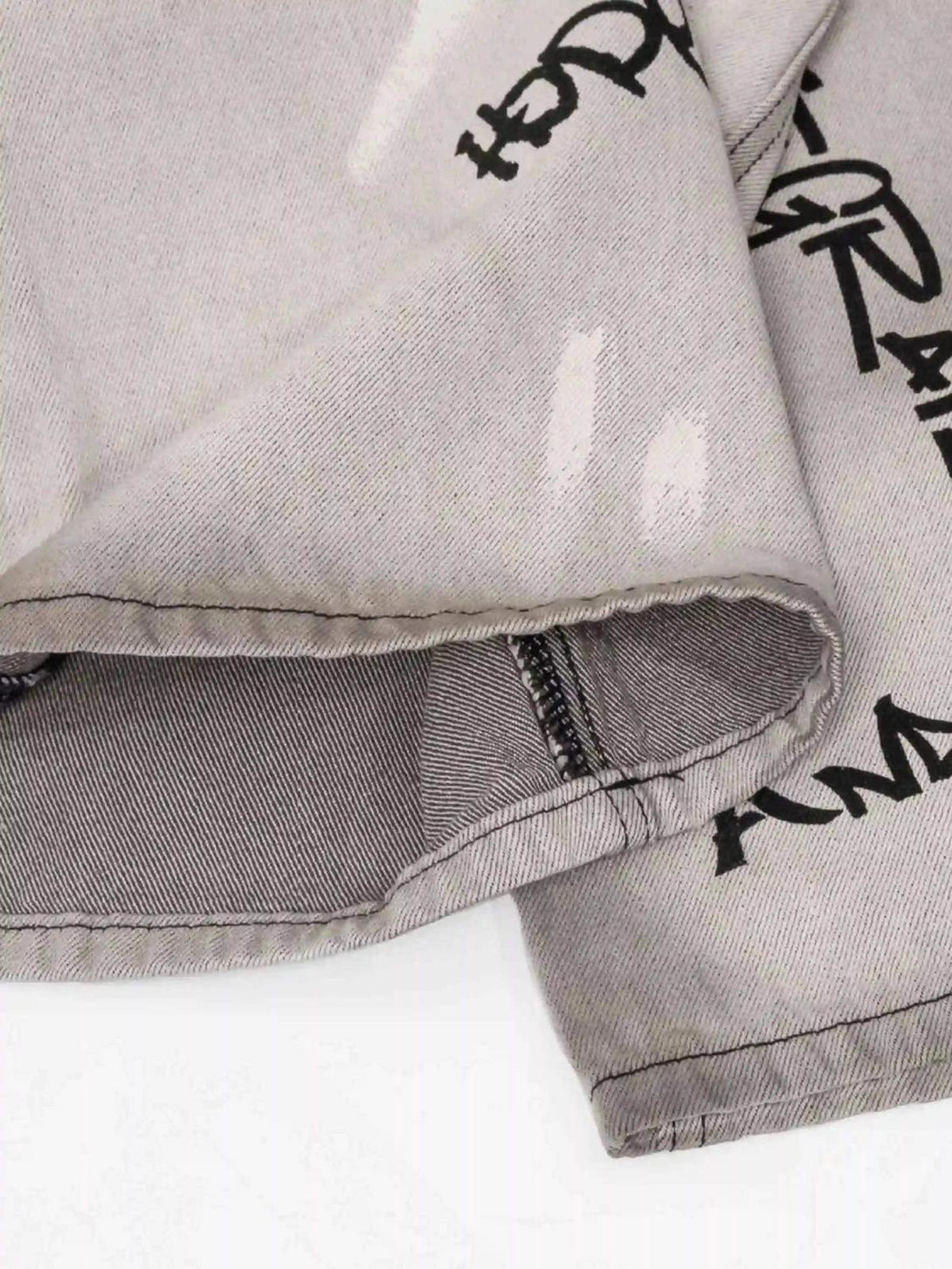 Detailed view of TALISHKO graffiti distressed jeans, highlighting bold black text and stitching.