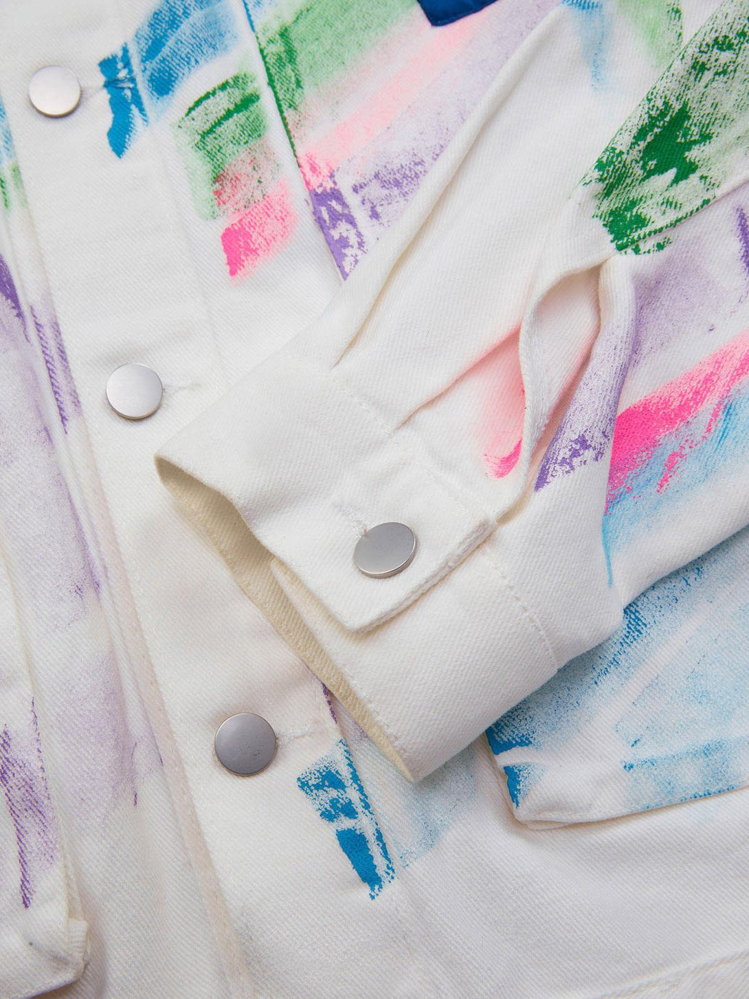 Detailed fabric view of TALISHKO's graffiti denim jacket with colorful brushstrokes and silver buttons.