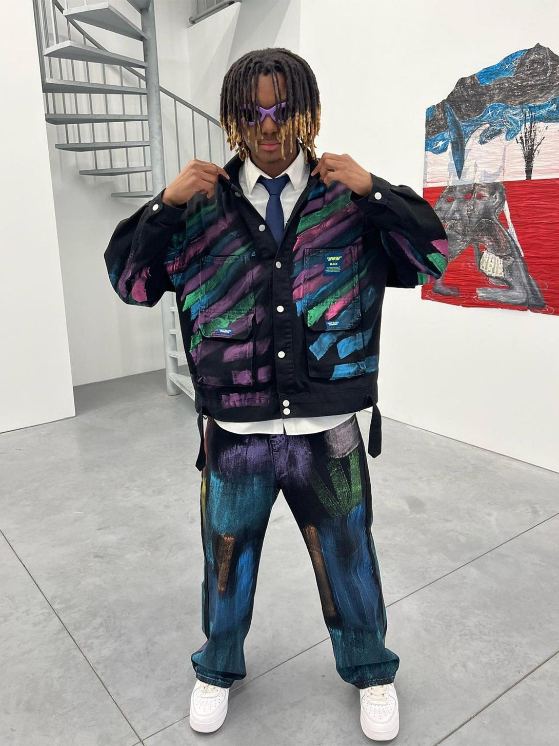 A model showcases a TALISHKO graffiti denim jacket with colorful hand-painted details, paired with matching pants.