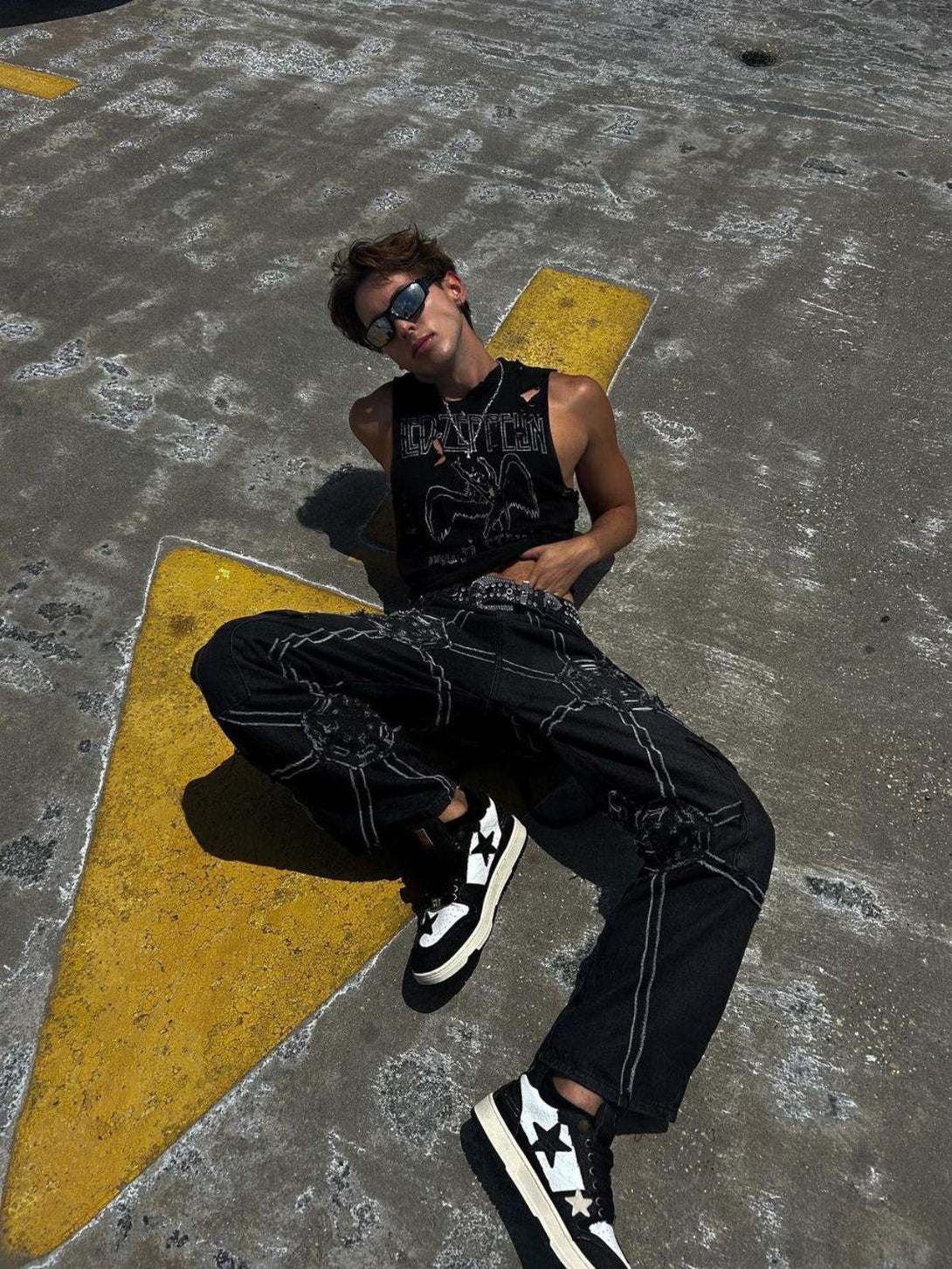 Model lounging in TALISHKO hip-hop jeans with spider web design, paired with stylish sneakers.