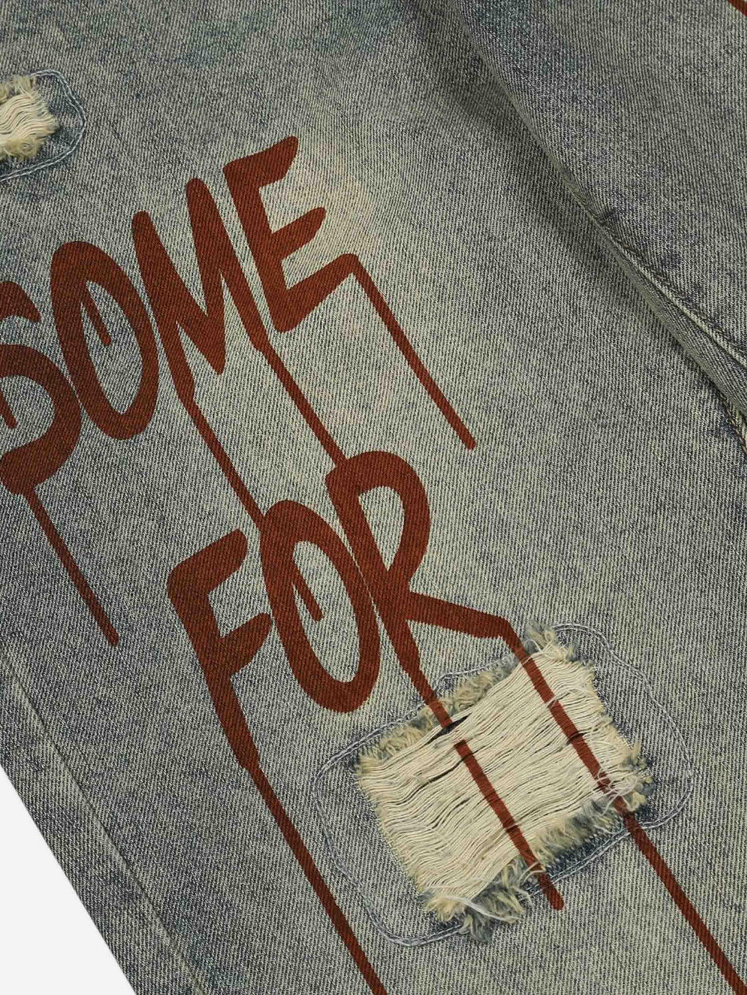 A detailed view of TALISHKO's denim jeans with bold text and distressed patch design.
