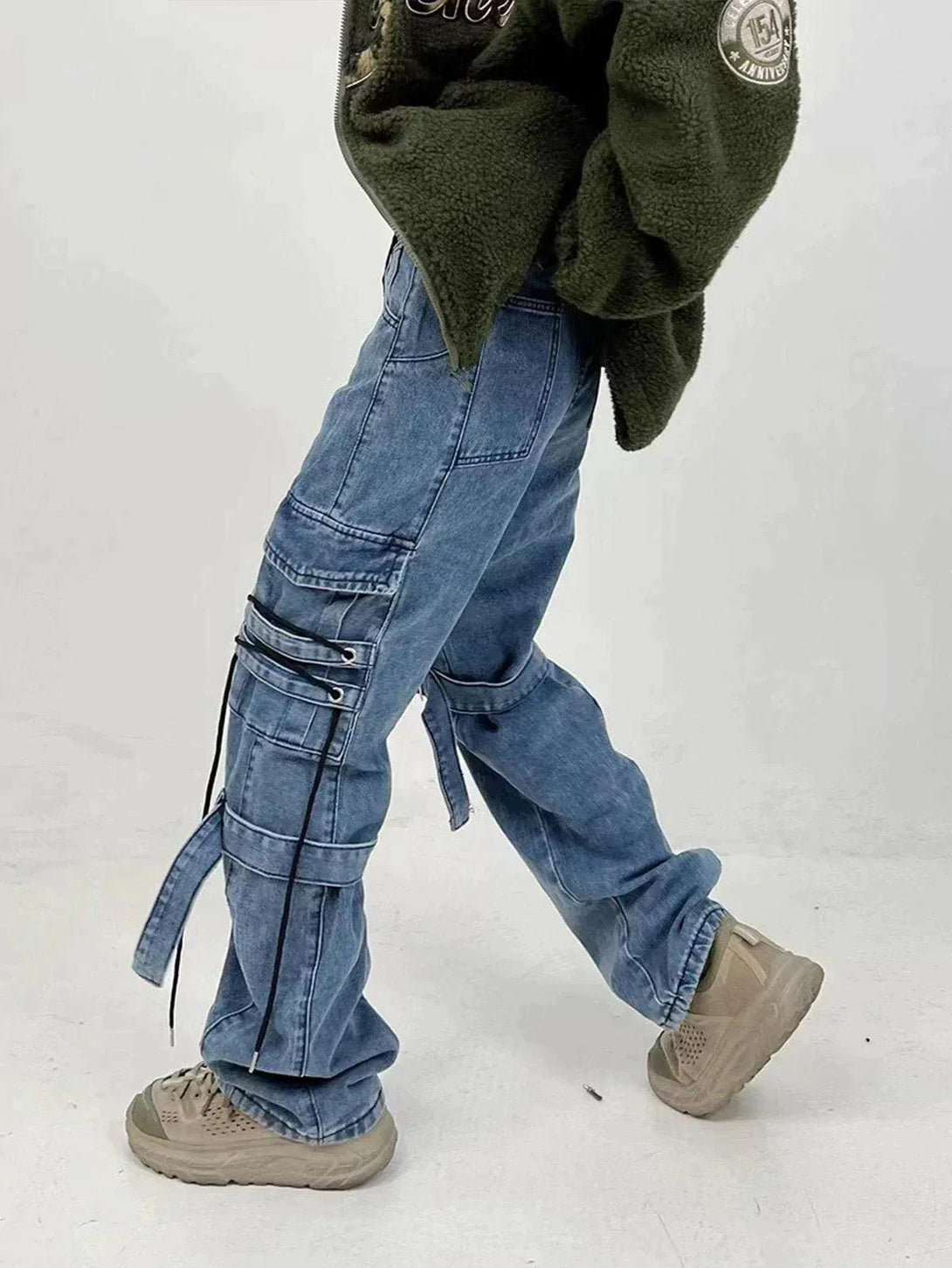 TALISHKO denim jeans with strap accents styled casually with an olive jacket and sneakers.