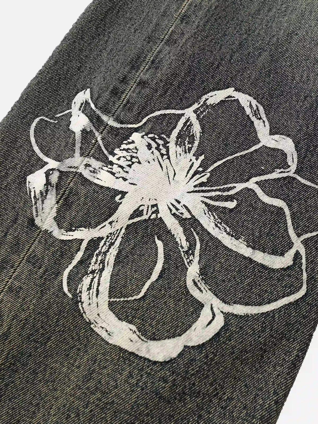 A close-up of TALISHKO graffiti jeans featuring a white floral design on dark denim fabric.