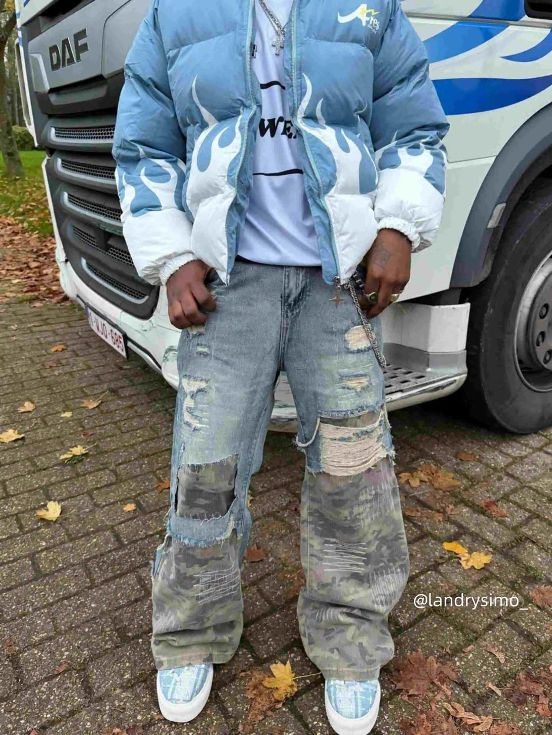 Model in TALISHKO's distressed jeans with camo patches, paired with a blue flame puffer jacket.