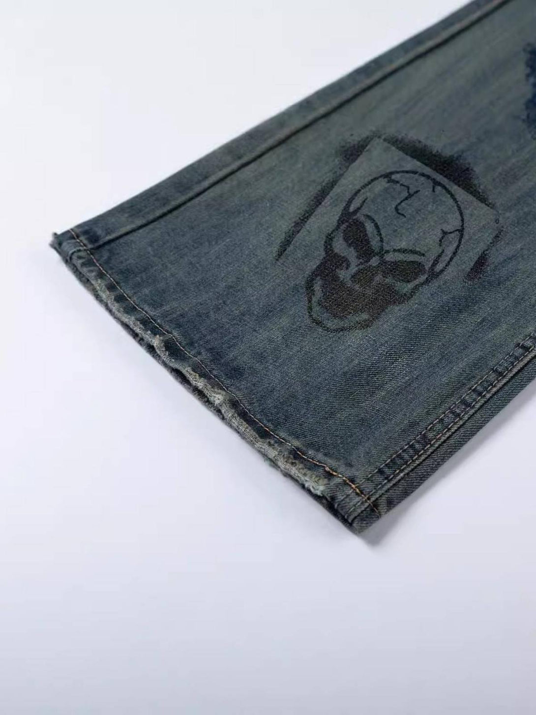 A close-up of TALISHKO jeans featuring a skull graffiti design and textured denim hem.