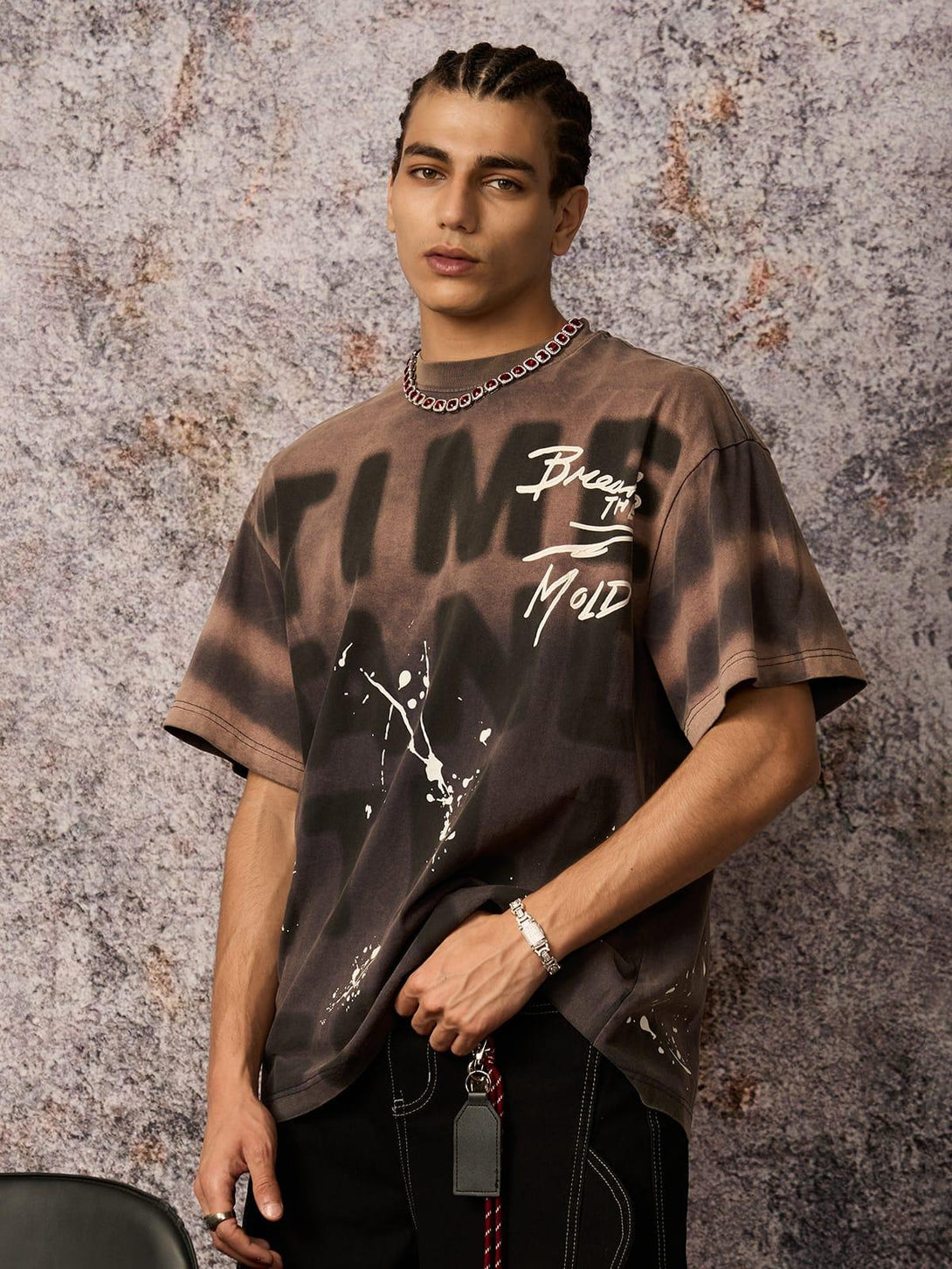 Model in TALISHKO ink splash letter print T-shirt, showcasing edgy urban style against textured backdrop.