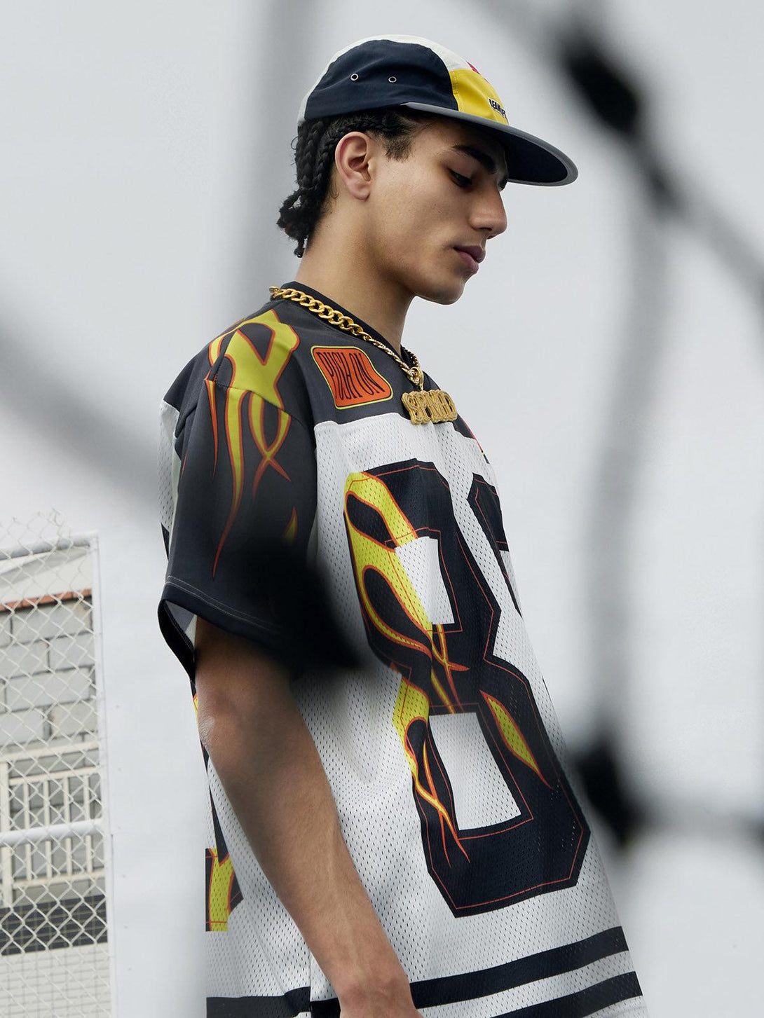 Model wearing a flame print jersey-style T-shirt by TALISHKO, paired with a trendy cap.