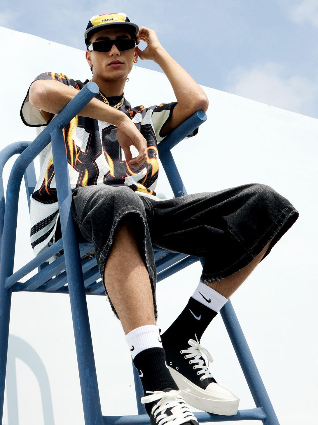 Model sitting on a blue chair wearing a flame print jersey-style T-shirt by TALISHKO.