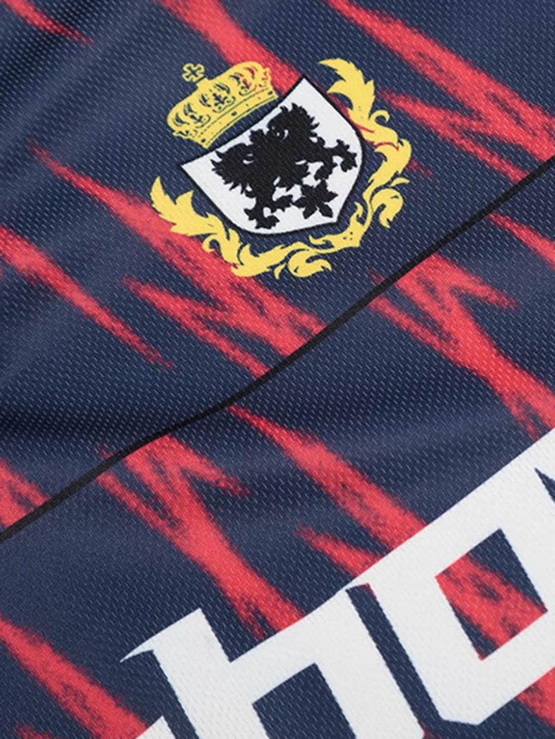 Detailed view of a TALISHKO jersey's crest and vibrant red patterns on navy fabric.