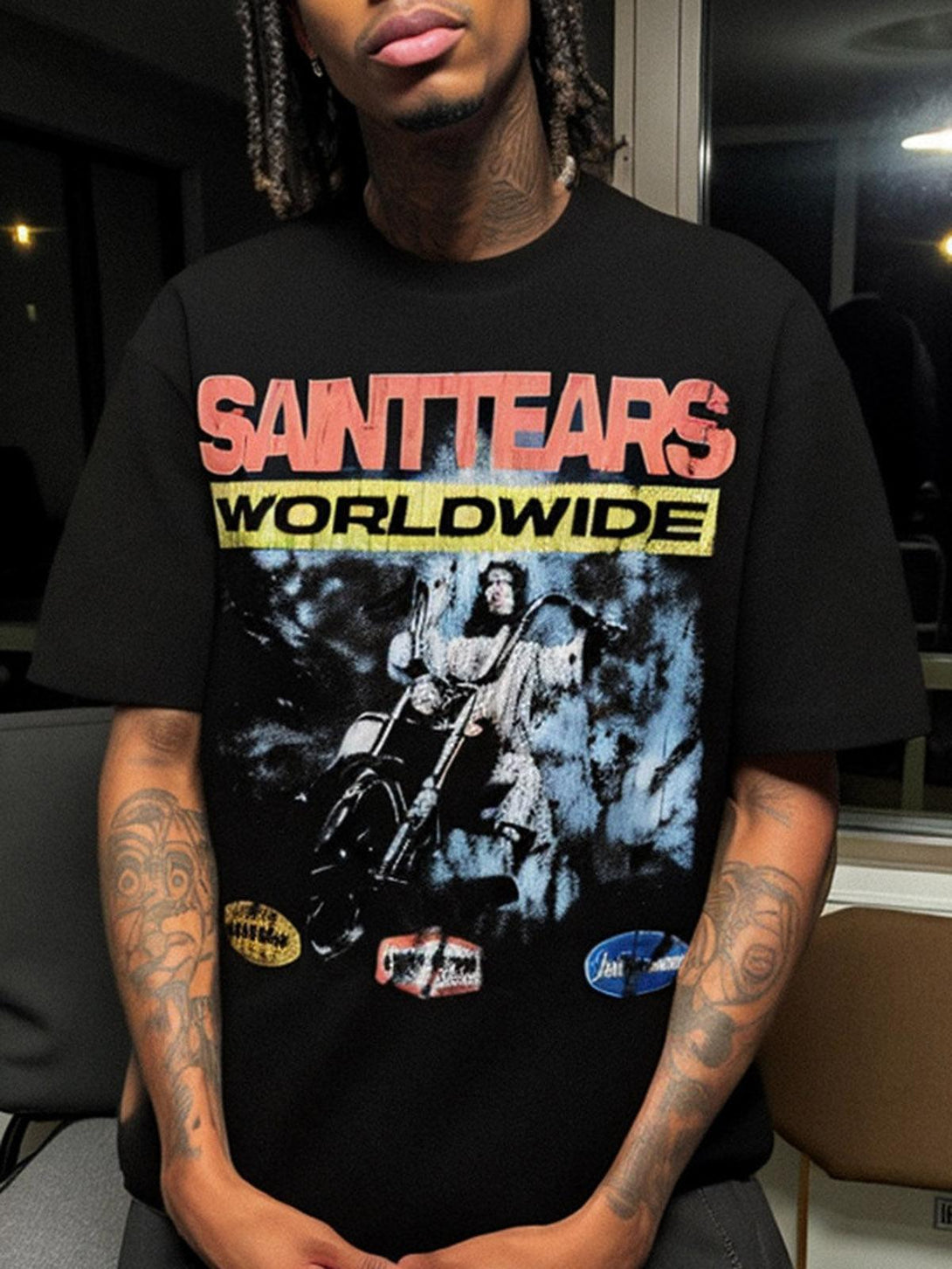 Model wearing black graphic T-shirt by TALISHKO with bold "SAINTTEARS" and "WORLDWIDE" text.