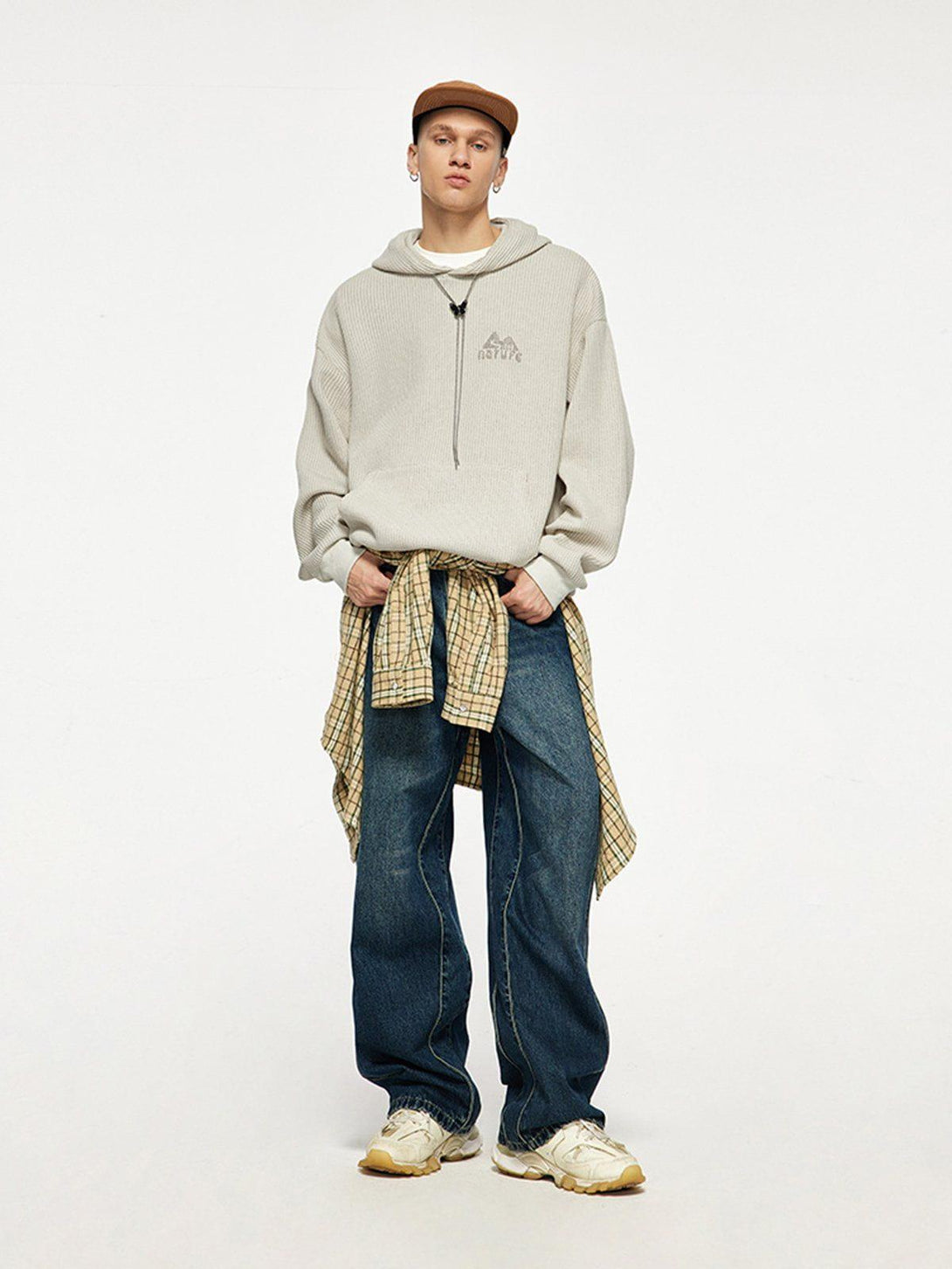 Model wearing a beige knit hoodie by TALISHKO, paired with jeans and a plaid shirt for a relaxed look.