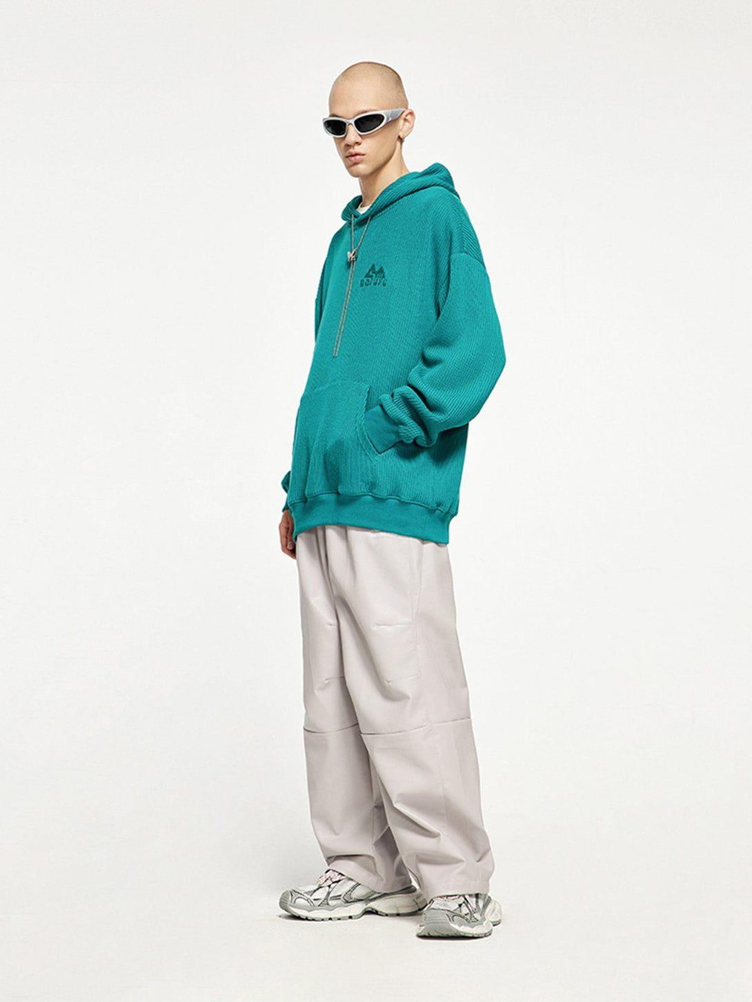 Model in teal knit hoodie by TALISHKO, paired with loose pants and sneakers for a trendy look.