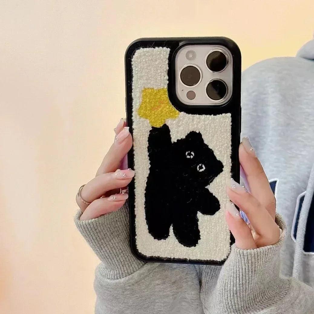 A TALISHKO plush iPhone case with a cute black bear design, held in a cozy setting.