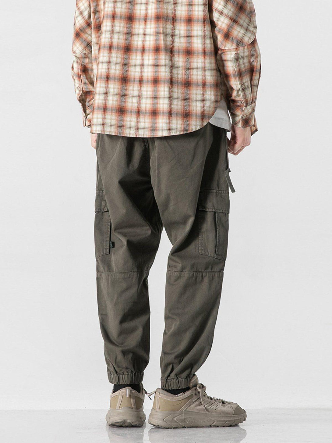 Model in TALISHKO cargo pants with multiple pockets, paired with plaid shirt and sneakers, back view.