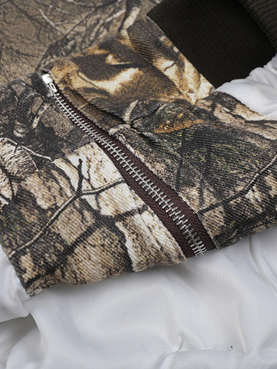 A detailed look at the zipper and fabric texture on a TALISHKO leaf camouflage bomber jacket.