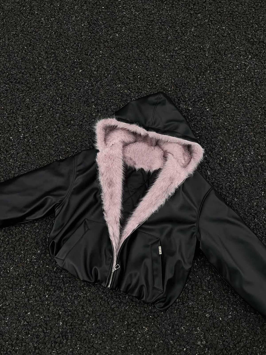 Black leather jacket featuring a pink fur hood by TALISHKO, arranged on a textured surface.