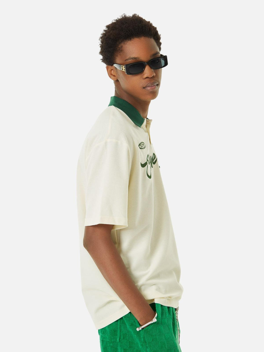 Model wearing a TALISHKO polo shirt with green embroidery and collar, paired with vibrant shorts.