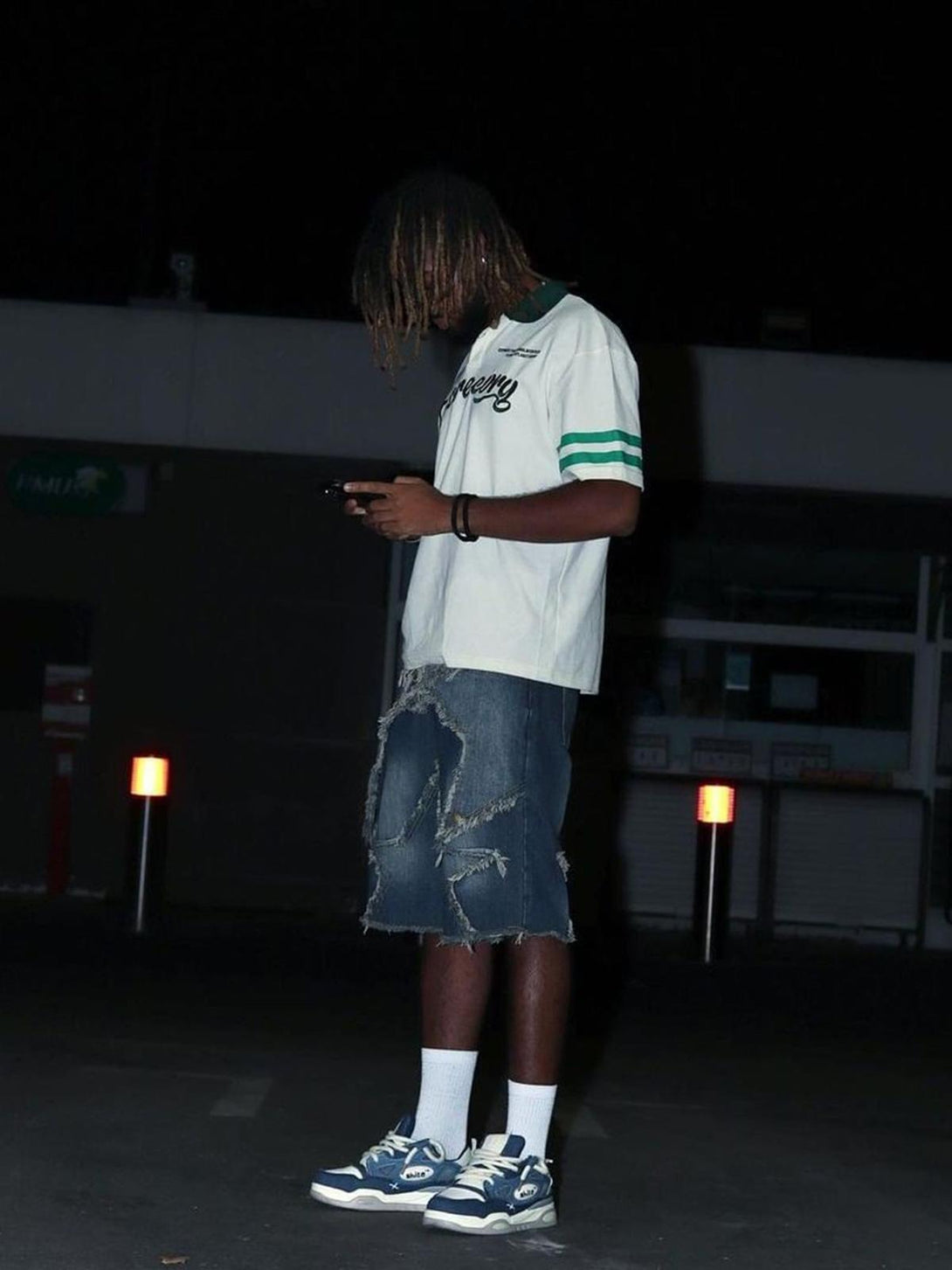 Model wearing a TALISHKO polo shirt with letter embroidery, paired with distressed denim shorts.