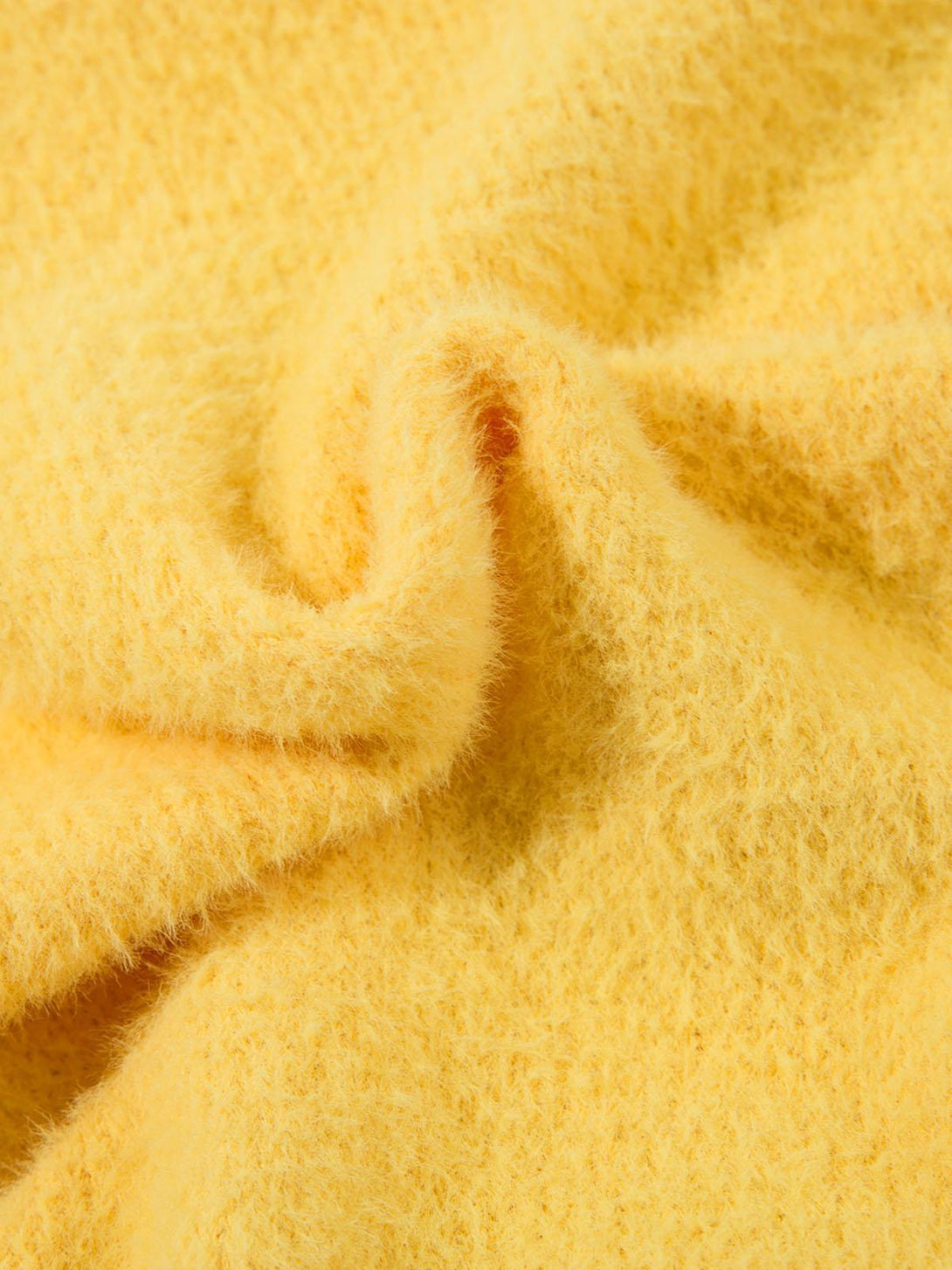 Focusing on the soft, fluffy texture of a yellow sweater by TALISHKO, highlighting its warmth.