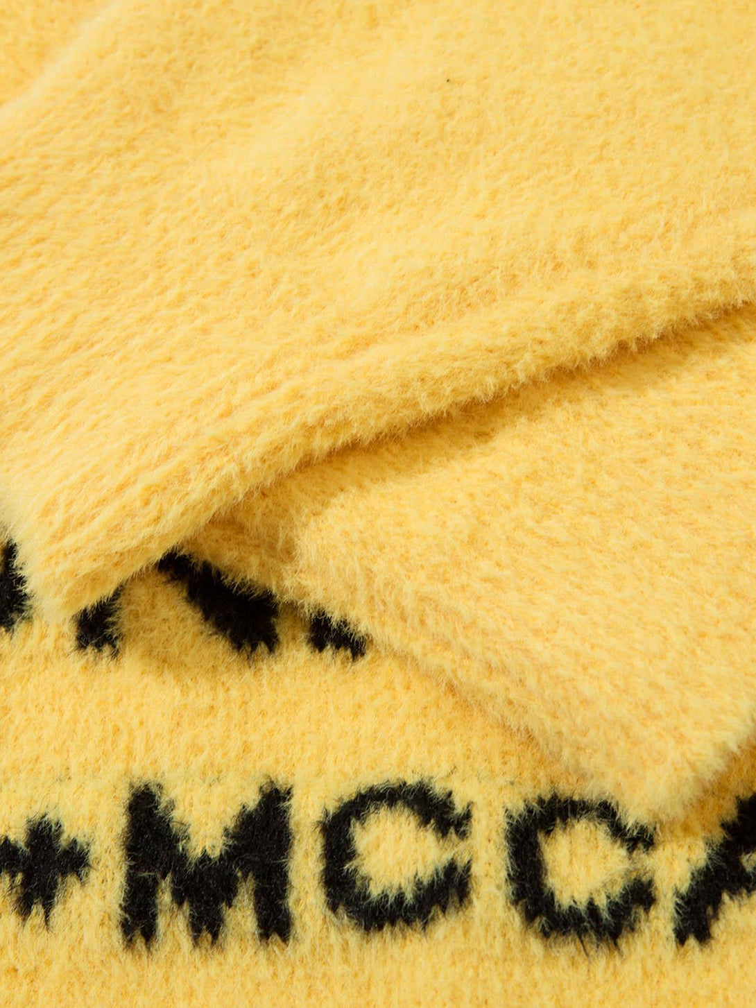 A detailed view of a yellow letter graphic sweater by TALISHKO, showcasing its plush texture.