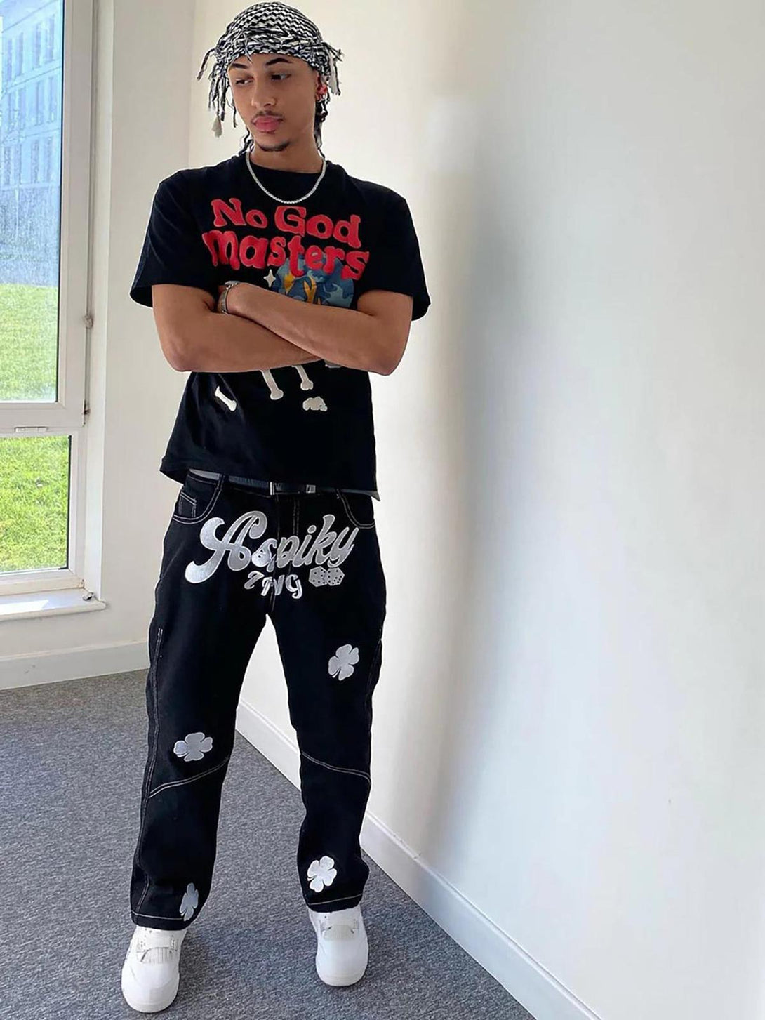 Model wearing TALISHKO's black baggy jeans with embroidered lucky clovers, styled casually indoors.