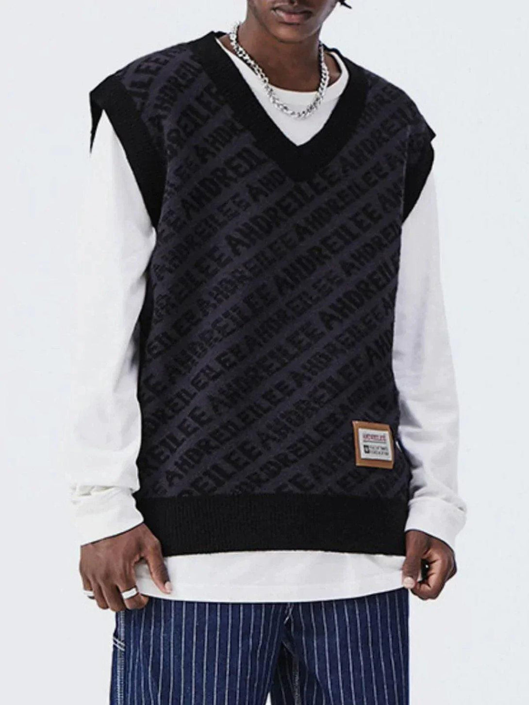 Model in a black letters graphic sweater vest by TALISHKO, styled with striped pants.