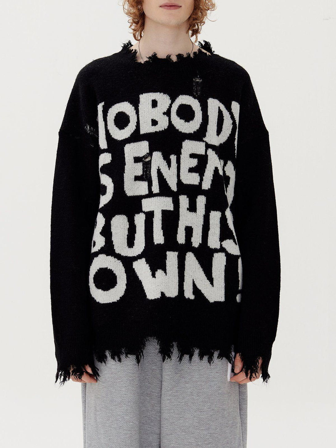 Model in black TALISHKO sweater with bold lettering and distressed edges, paired with gray pants.