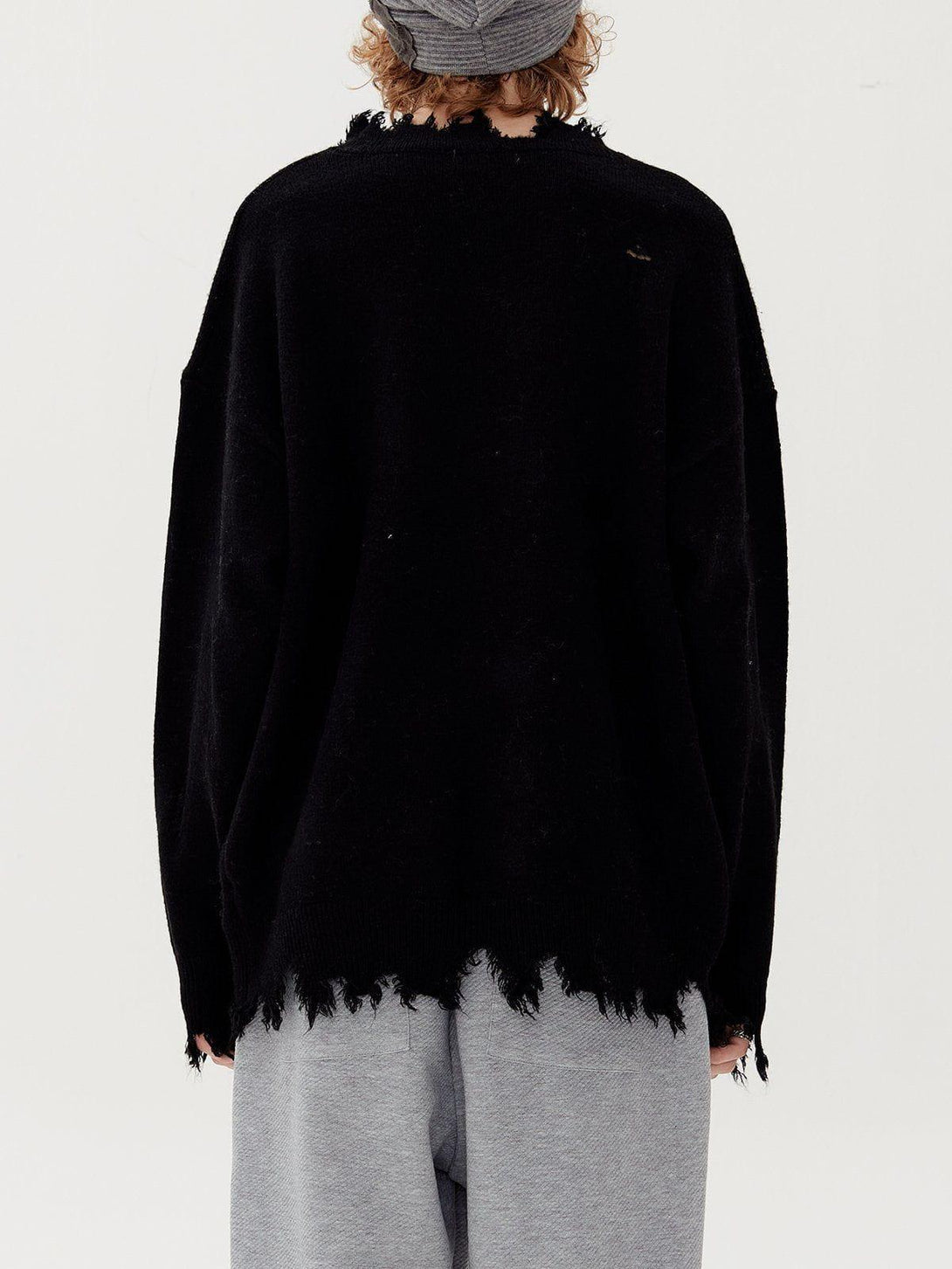 Back view of a black TALISHKO ripped hole sweater with distressed edges, paired with gray pants.