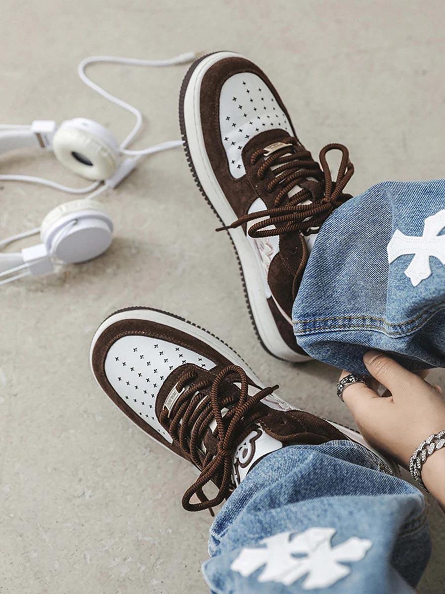Brown and white TALISHKO skate sneakers with cross patterns, styled with blue jeans and headphones.