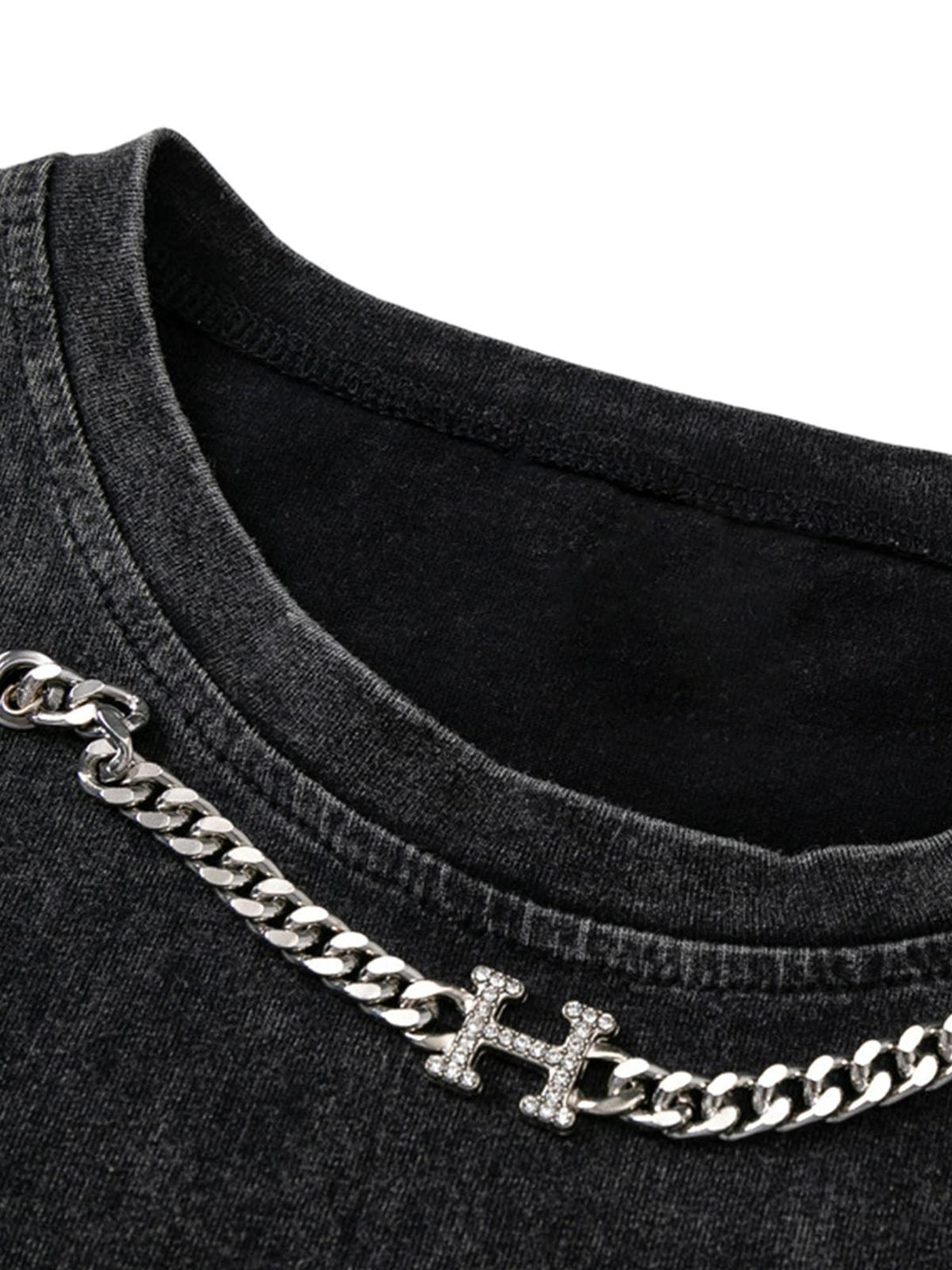 Close-up of TALISHKO vest neckline with chain detail featuring a crystal-studded "H" accent.