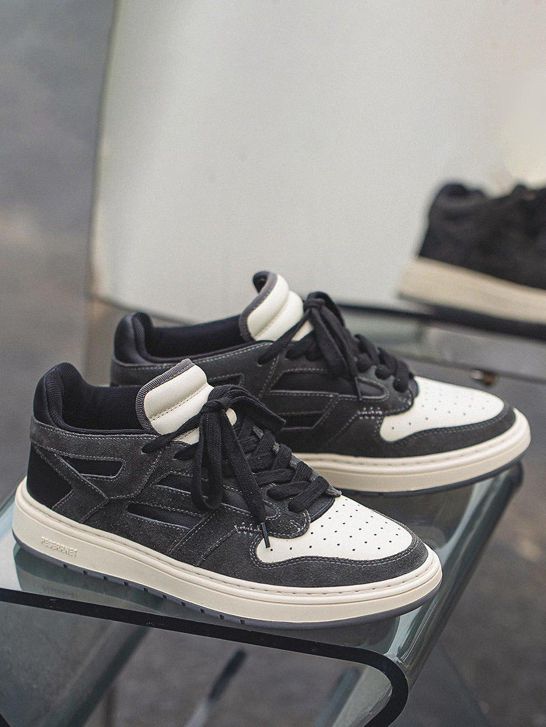 TALISHKO low-top sneakers feature a black and white design, elegantly displayed on a glass surface.