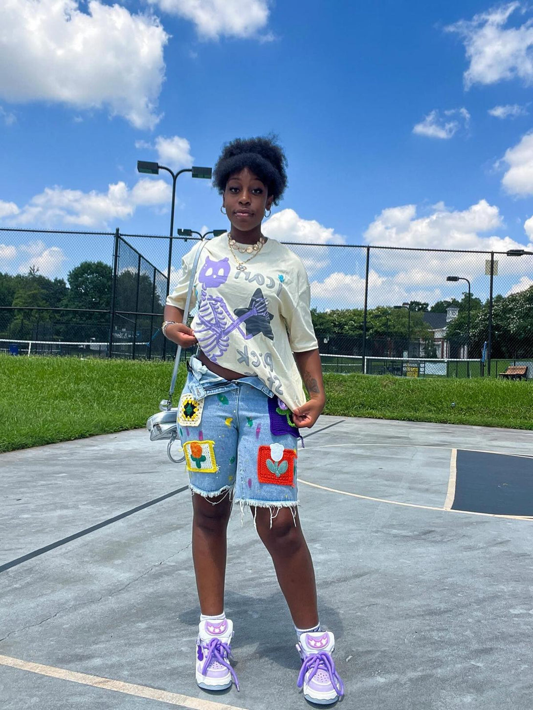 Model in TALISHKO graphic T-shirt with skeleton design, paired with colorful patch shorts outdoors.