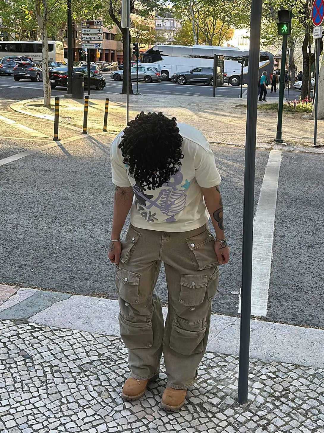 Model wearing a TALISHKO graphic T-shirt with skeleton design, styled with cargo pants outdoors.