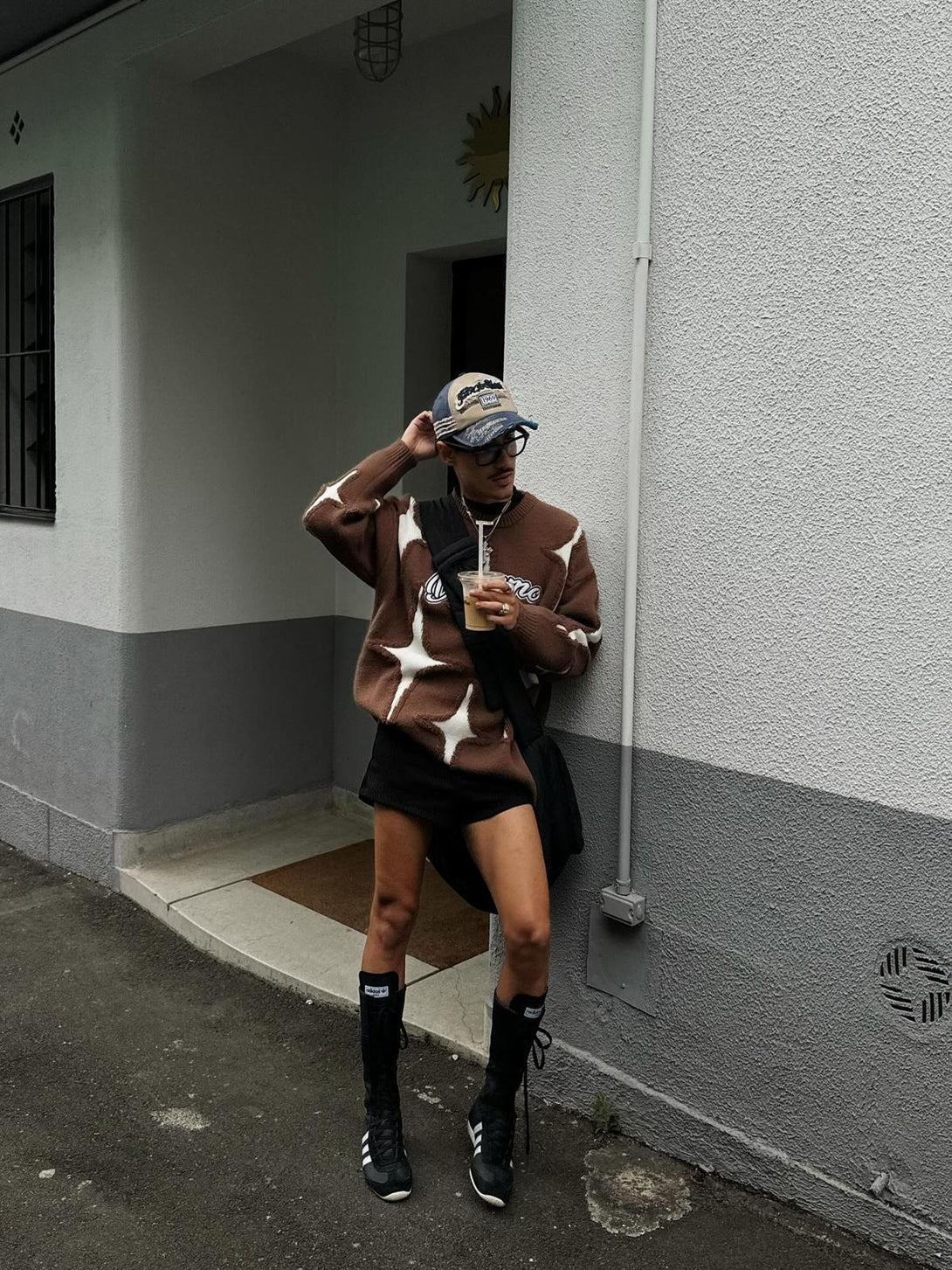 Model wearing TALISHKO's brown star-pattern sweater with tassels, styled with a cap and boots.