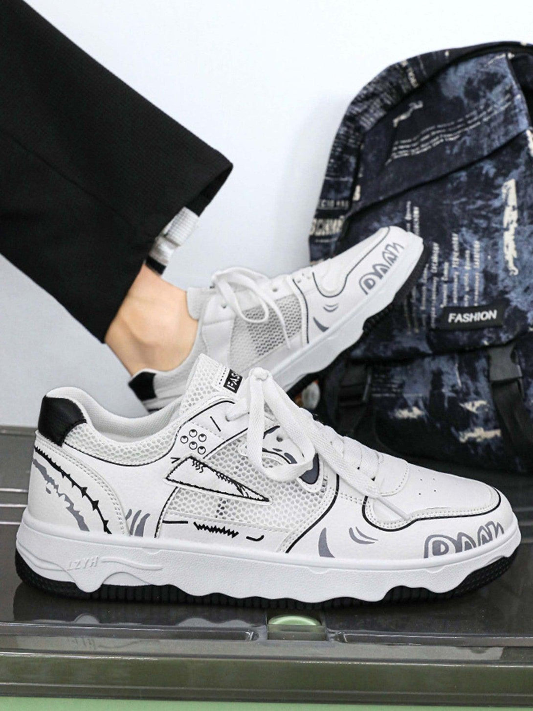 White mesh board shoes by TALISHKO featuring bold graphics, styled with casual trousers.