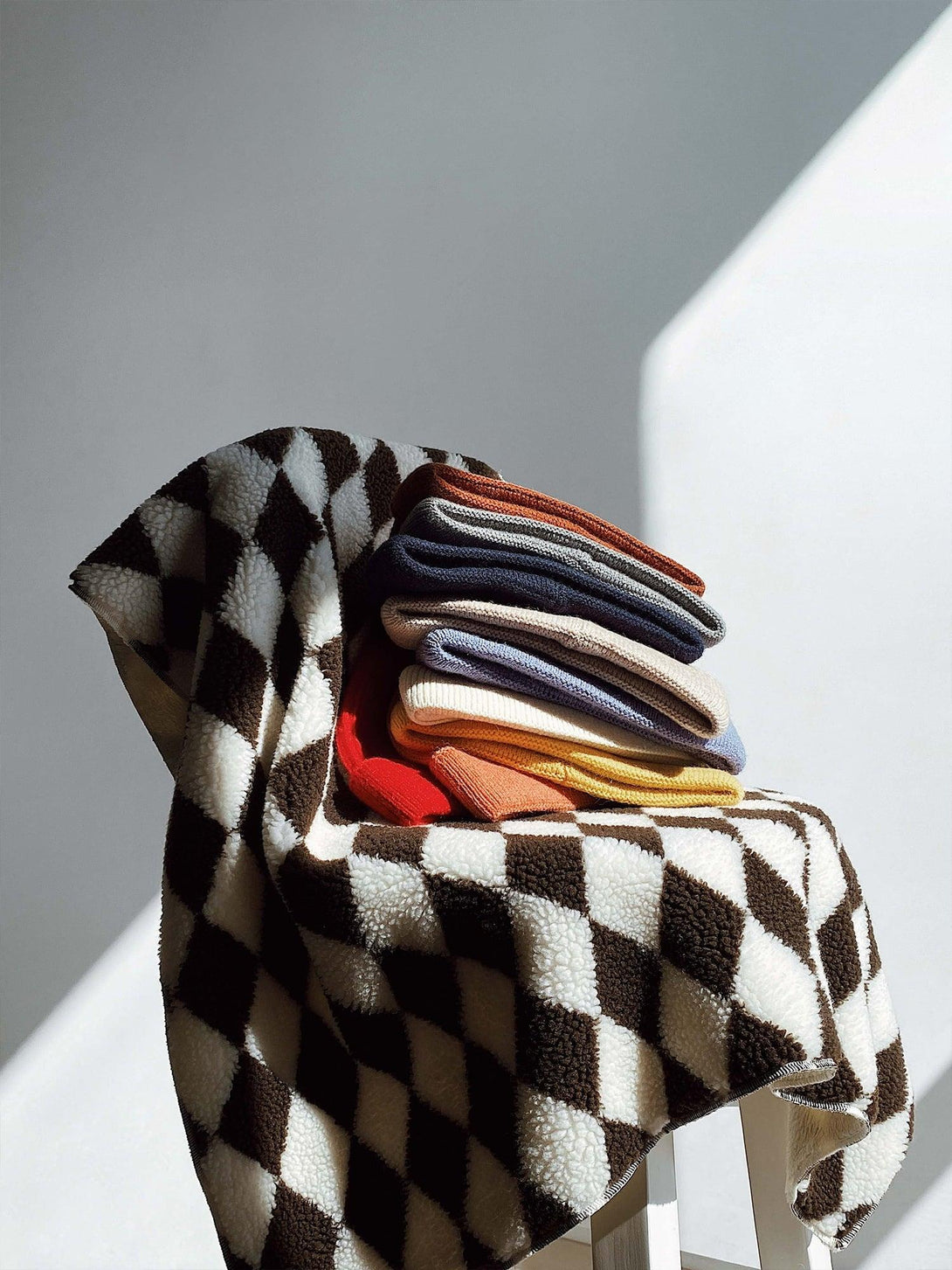 A stack of colorful mini fisherman beanies by TALISHKO, displayed on a checkered blanket.