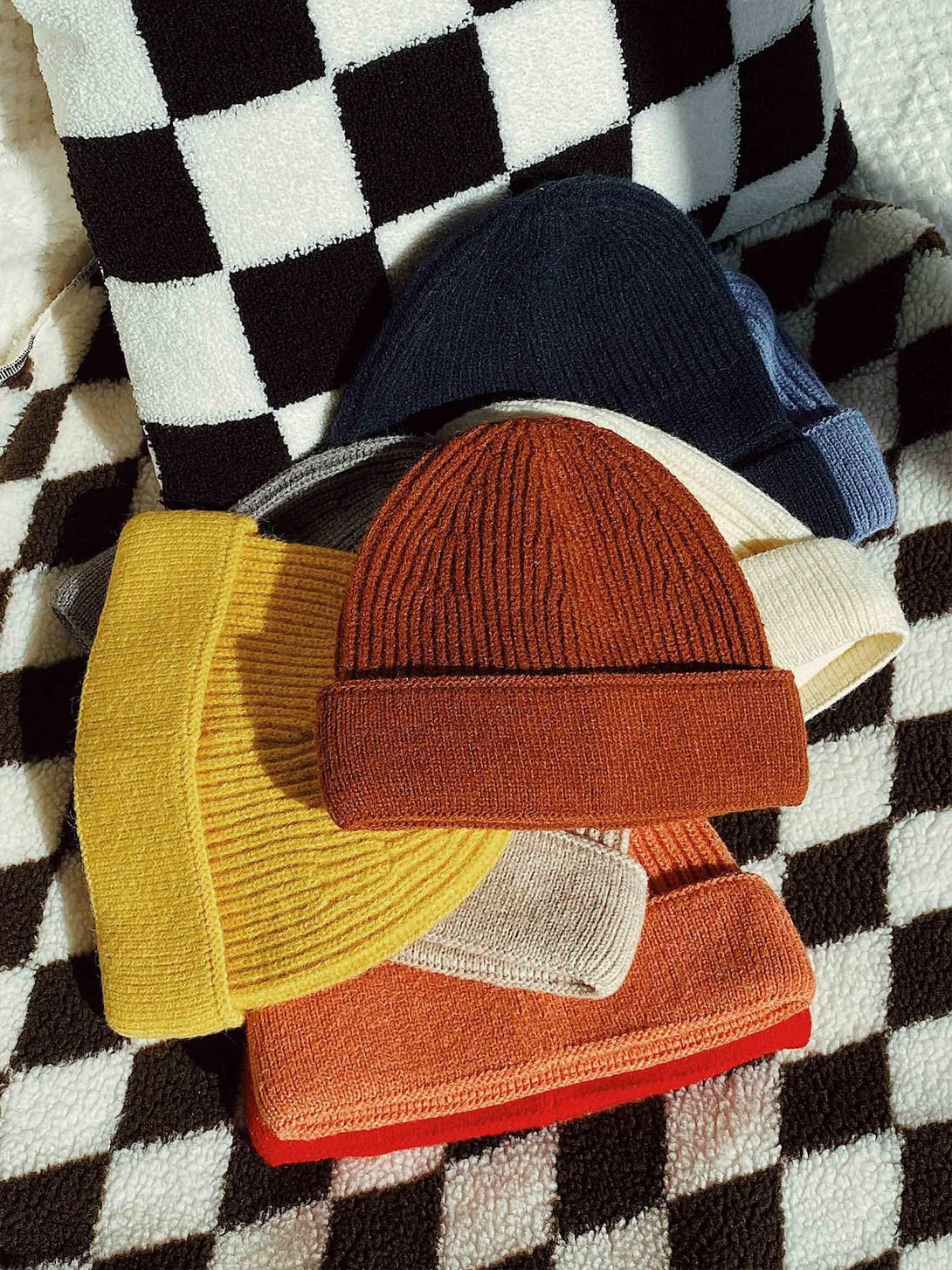 A vibrant stack of TALISHKO mini fisherman beanies on a stylish checkered blanket.