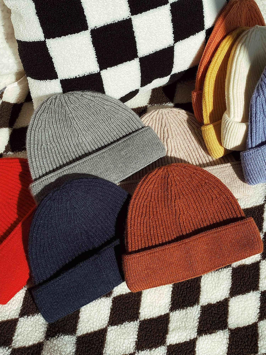 A vibrant collection of TALISHKO mini fisherman beanies on a bold black and white checkered fabric.