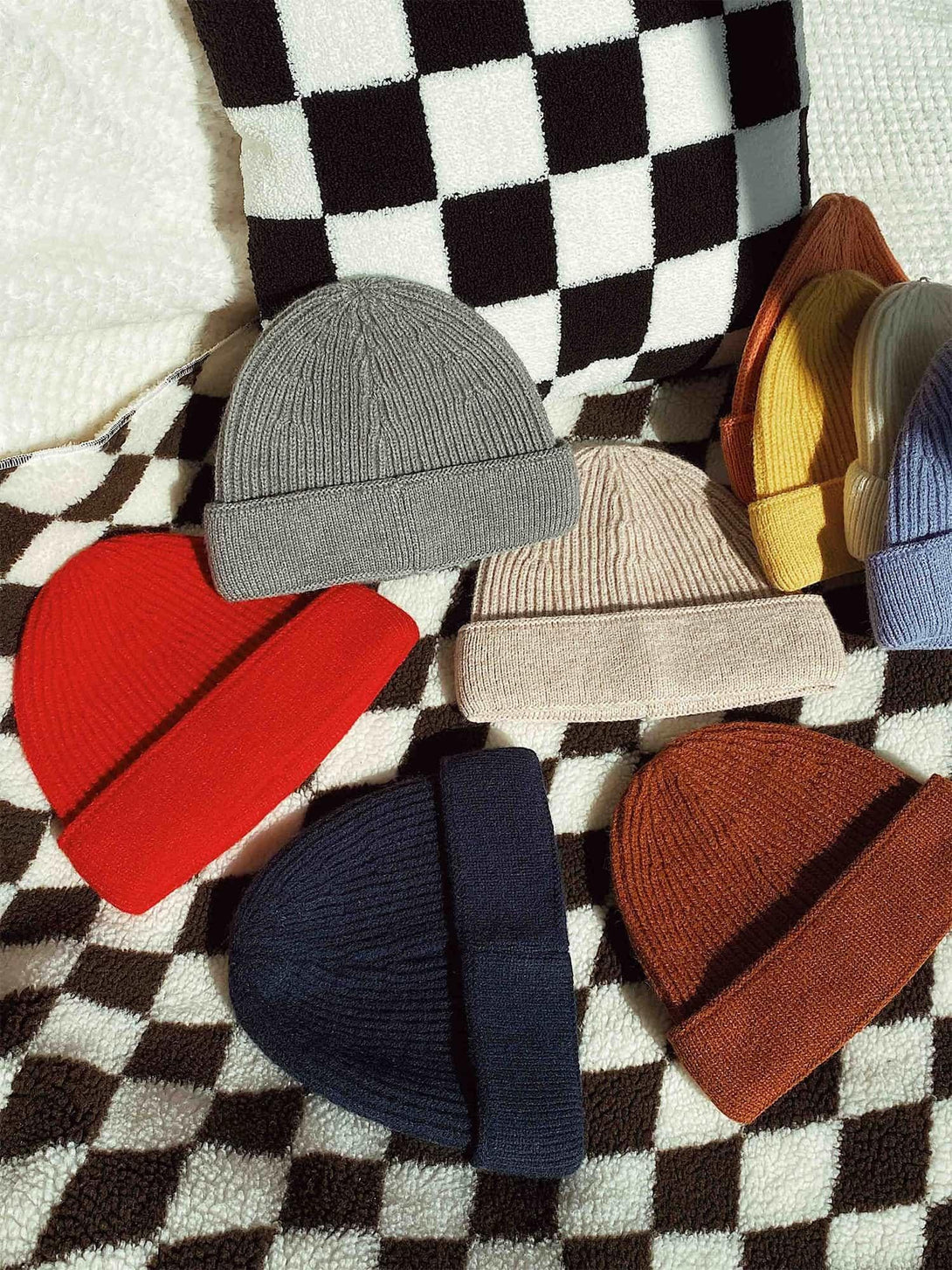 A colorful array of mini fisherman beanies by TALISHKO on a checkered background, showcasing cozy knit textures.