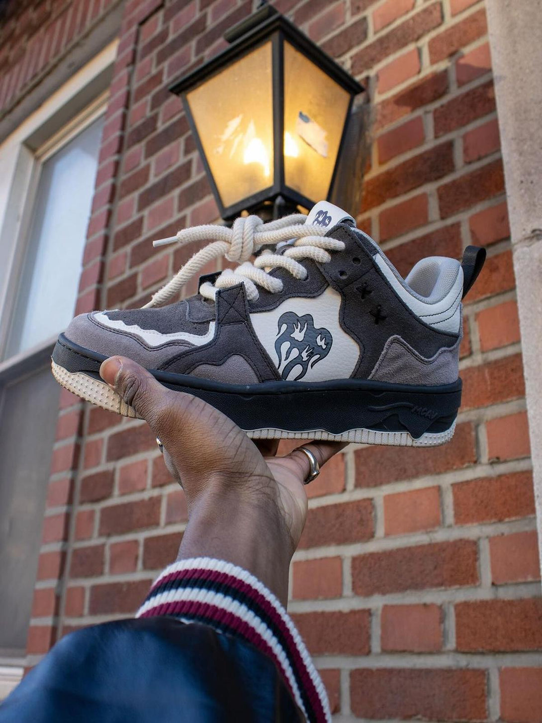 TALISHKO sneakers held up against a brick wall, highlighting their monochrome street style.