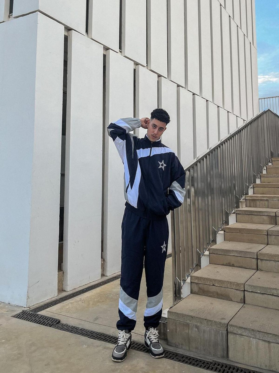 Model in a sporty tracksuit and TALISHKO sneakers, standing by modern architecture.