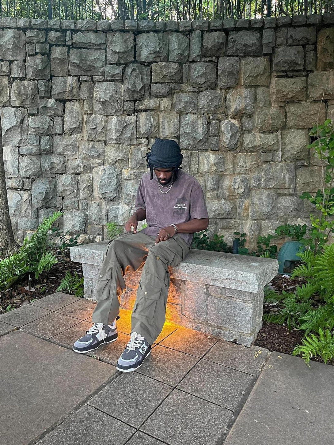 Casual outdoor look featuring TALISHKO sneakers, cargo pants, and a relaxed tee on a stone bench.