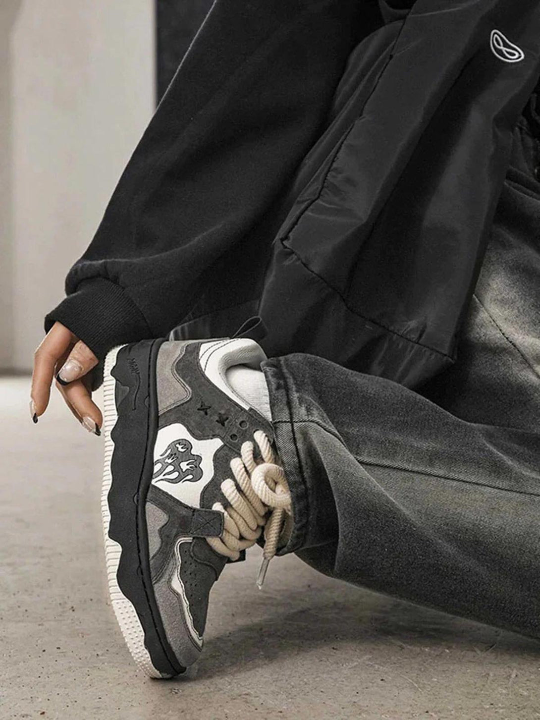 A close-up of TALISHKO sneakers with bold laces and intricate monochrome design against dark jeans.