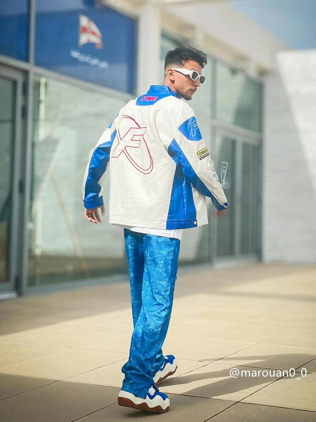 A stylish model wearing a TALISHKO racing jacket, showcasing bold blue and white design elements.