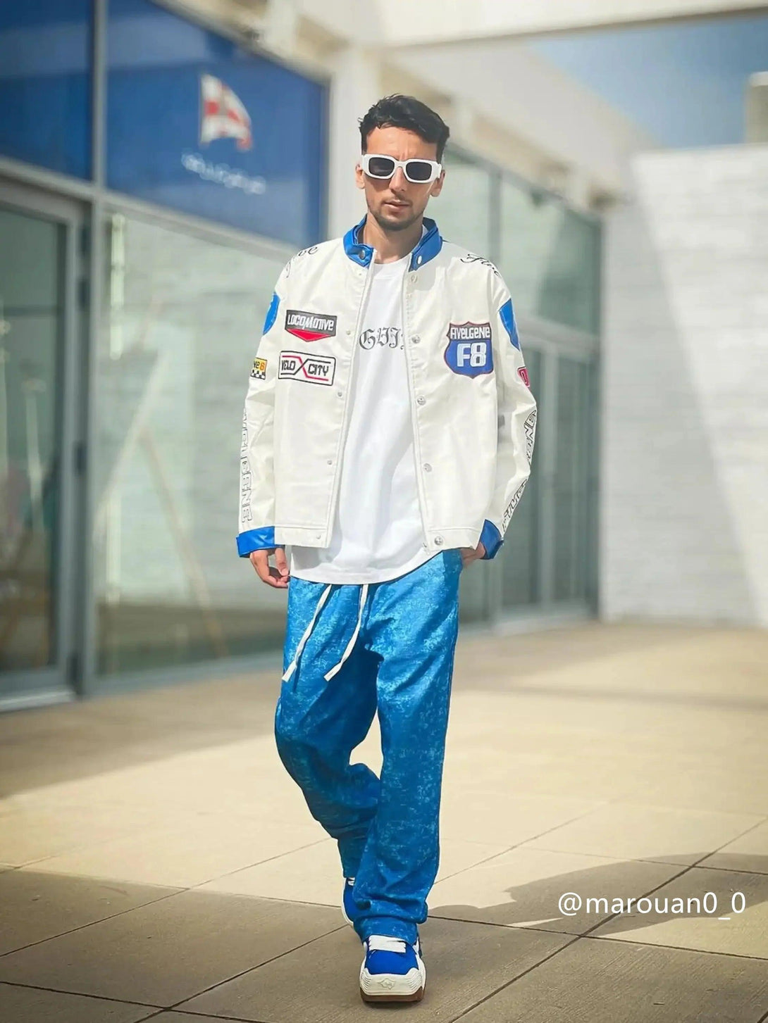 Model wearing a TALISHKO racing jacket with bold patches and vibrant blue pants for a dynamic look.